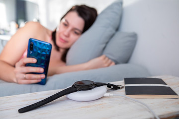 woman surfing internet on cellphone laying in bed smart watch on wireless charger