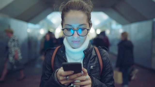 Woman standing in the entrance of a subway station using a smartphone while people walk around her