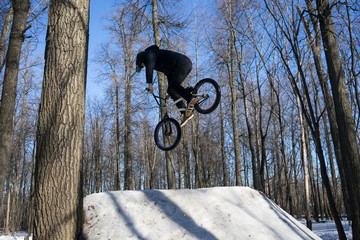 A cyclist does a 360 trick on a springboard in winter. Athlete shows a trick on a bicycle.