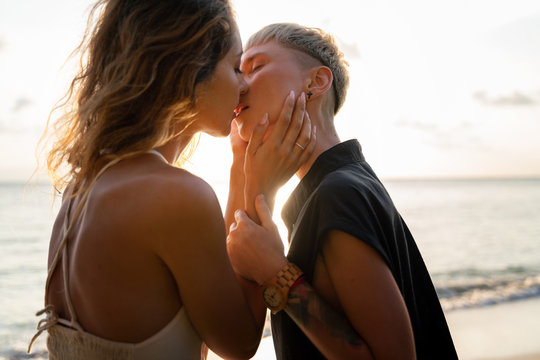 Two beautiful young women gently passionately kiss their lips on the beach during a wedding and honeymoon in the tropics. In the rays of the setting sun. Love tenderness attraction concept
