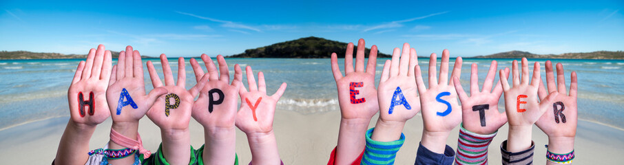 Children Hands Building Colorful Word Happy Easter. Ocean With Sandy Beach As Background