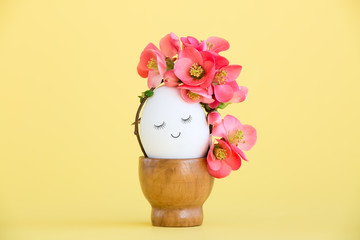 Cute egg with a painted face and spring flowers on a yellow background. Creative concept for Easter