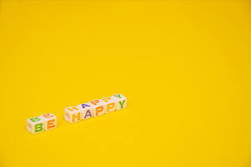 Colored cube letters with words "Be happy" yellow background with mockup space. Tilted view