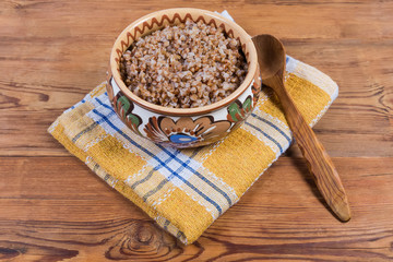 Buckwheat porridge in clay bowl, wooden spoon on rustic table