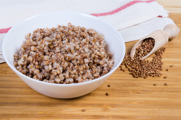 Prepared buckwheat porridge and uncooked buckwheat groat on wooden surface