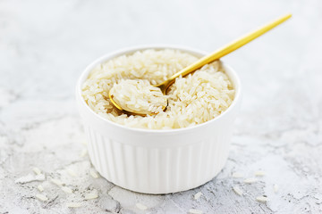 Rice in a bowl with a spoon on a gray background. Gluten free, healthy diet concept.
