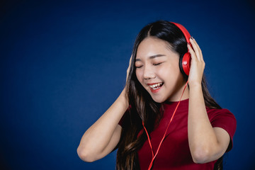 Happy cheerful Asian beautiful woman wearing Red headphones or earphone speaker listening to music from smartphone with smile. Studio shot isolated on blue background.