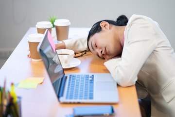Working Asian woman feeling drowsy and sleeping on desk in office due to overload job.  Working...