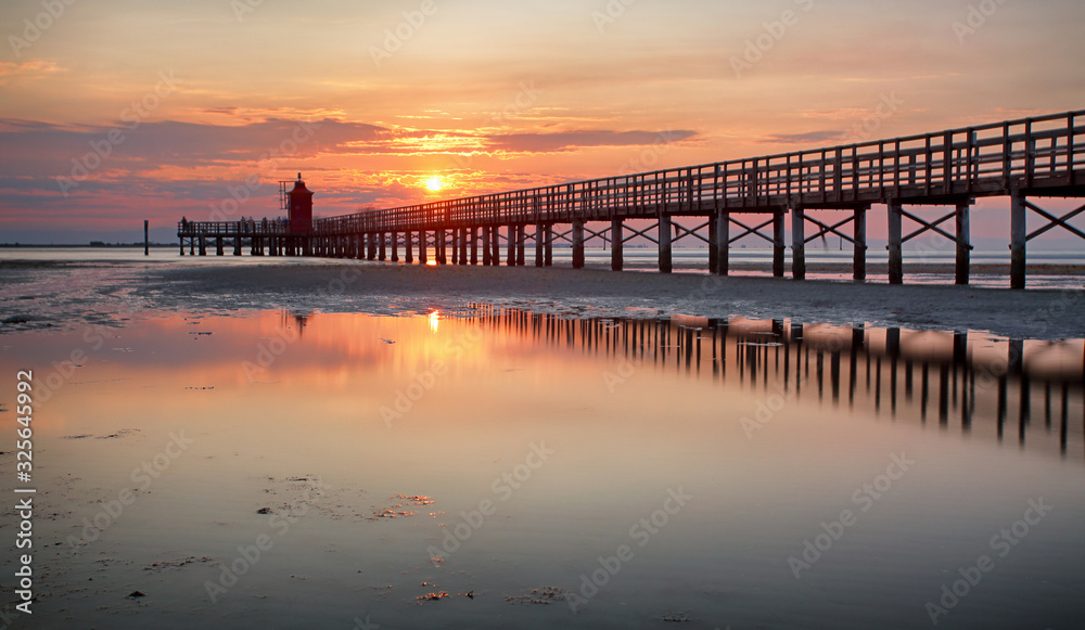 Wall mural Wooden pier leading to a red lighthouse at sunrise in Lignano Sabbiadoro, Friuli, Italy - beach