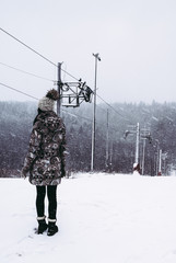 Woman in winter coat standing on slope near loop-line ski lift during snowfall. beautiful winter...