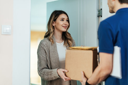 Smiling woman receiving a package from delivery man at home.