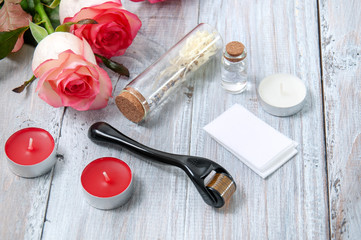Pink roses, oil bottles, facial masseur and candles on a gray wooden table. March 8. Valentine's Day. Greeting card. Romantic and beautiful background. Spa treatments. Personal care. Love and beauty.
