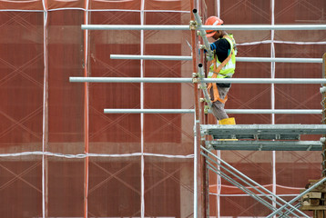 Construction workers wearing safety harness and installing scaffolding at high level in the...