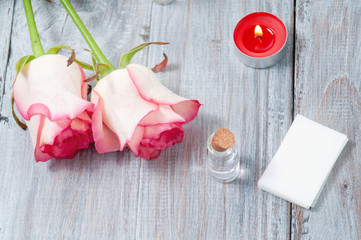 Pink roses, oil bottles and candles on a gray wooden table. March 8. Valentine's Day. Greeting card. Romantic and beautiful background. Spa treatments. Personal care. Love and beauty.