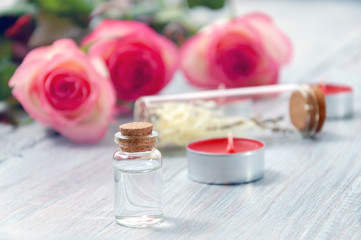 Pink roses, oil bottles and candles on a gray wooden table. March 8. Valentine's Day. Greeting card. Romantic and beautiful background. Spa treatments. Personal care. Love and beauty.