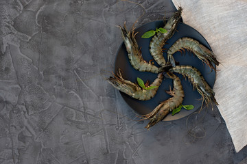 Fresh raw shrimp prawns on a black plate on a gray concrete background. Healthy seafood is a source of protein. Flat lay. Copy space.
