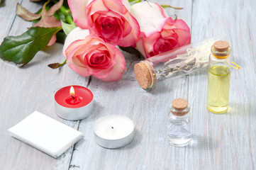 Fototapeta na wymiar Pink roses, oil bottles and burning candles on a gray wooden table. March 8. Valentine's Day. Greeting card. Romantic and beautiful background. Spa treatments. Personal care. Love and beauty.