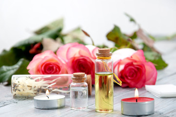 Pink roses, oil bottles and burning candles on a gray wooden table. March 8. Valentine's Day. Greeting card. Romantic and beautiful background. Spa treatments. Personal care. Love and beauty.