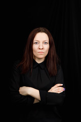 Portrait of successful business woman in 
a black shirt with crossed hands on black background