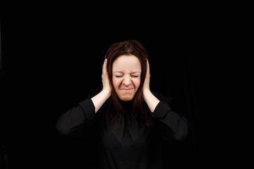 Confused woman holding hands on head over black studio background. Portrait of young serious girl closing her ears, hear no evil, deafness concept, copy space