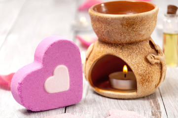 Aroma lamp with a burning candle and essential oils, pink salt bath bomb in the form of a heart, rose petals on a gray wooden table.  Face and body care. Spa treatments.