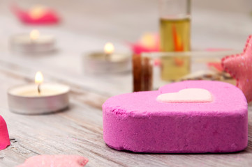 Obraz na płótnie Canvas Essential oils, pink salt bath bomb in the form of a heart, rose petals on a gray wooden table. Face and body care. Spa treatments.