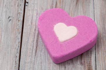 Obraz na płótnie Canvas Pink salt bath bomb in the shape of a heart on a gray wooden table. Face and body care. Spa treatments. Romantic background. Declaration of love. Valentine's Day.