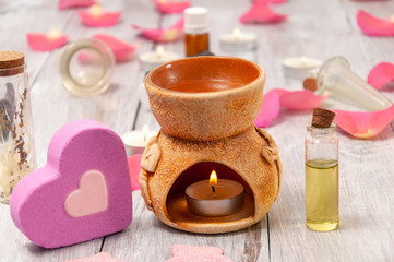 Aroma lamp with a burning candle and essential oils, pink salt bath bomb in the form of a heart, rose petals on a gray wooden table.  Face and body care. Spa treatments.
