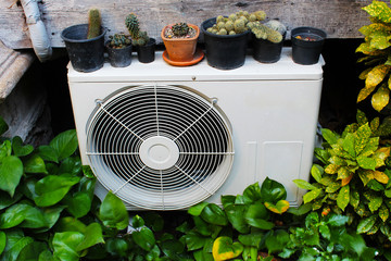 A compressor of air conditioner surrounded by beautiful plants