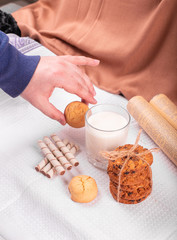 A glass of milk with caramel cookies and waffle sticks. man taking a cookie