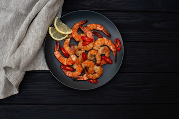 Tasty cooked fried shrimp with chilli and lemon on a black wooden background. Healthy seafood. Copy space. Flat lay.