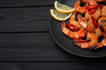 Tasty cooked fried shrimp with chilli and lemon on a black wooden background. Copy space. Flat lay.