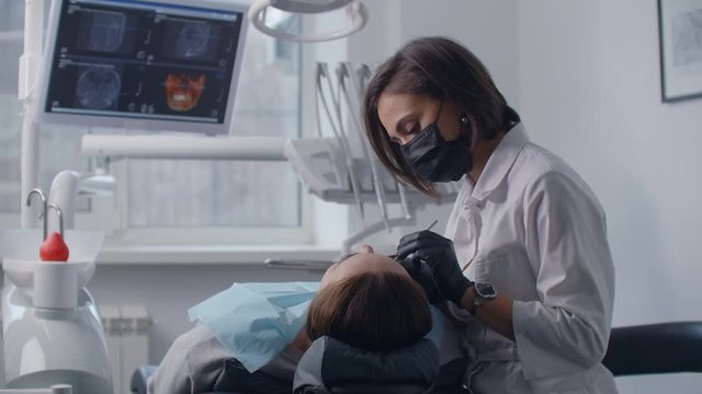 A dentist treats a patient lying in a chair on the background of a picture on the screen. Professional dentist