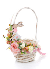Fototapeta na wymiar Little white round wicker basket with high handle. Basket decorated with delicate pink floral decor with decorative wooden hare on white background.