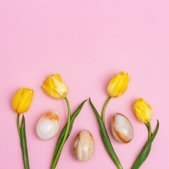 Bright blooming flowers and decorative easter eggs from gemstone onyx. Pattern from yellow tulips and stone eggs and with copy space. Holiday spring concept.