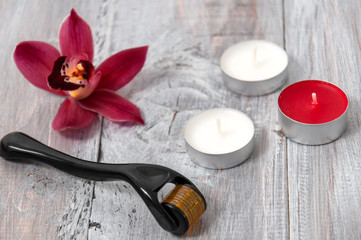 Obraz na płótnie Canvas Candles, orchid and facial massager on a gray wooden table. March 8. Face care. Spa treatments.