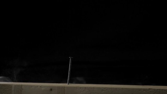 A Hammer Hitting a Nail with Dust Flying in Slow Motion (180 FPS) in front of Black Background.
