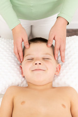 Obraz na płótnie Canvas Kids massage concept background. Female therapist giving a young boy face massage. Top view.