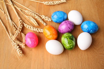 boiled colored eggs lie on a wooden table against the background of ripe ears of wheat, Easter concept
