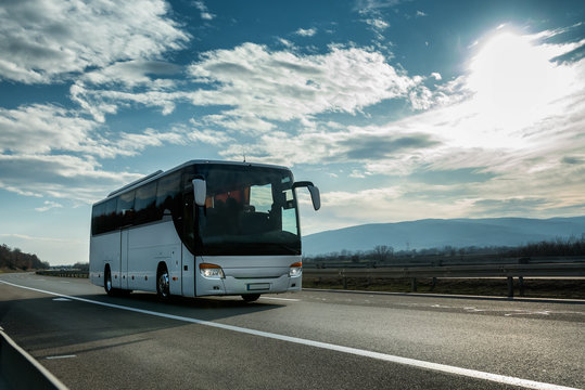 White Modern comfortable tourist bus driving through highway at bright sunny sunset. Travel and coach tourism concept. Trip and journey by vehicle