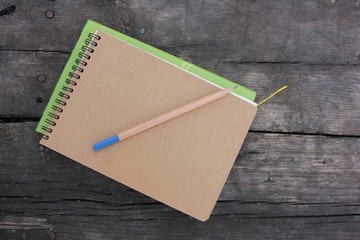 Book, paper notepad on spiral and pencil on rough textured wooden table in park. Top view