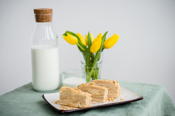 Piece of napoleon cake. Classic layered russian cake.  French mille feuille with whipped sour cream. Yellow tulips on table. 