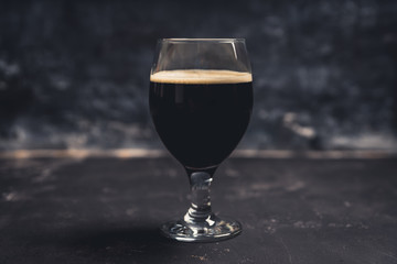 Freshly brewed dark beer on the black rustic background. Selective focus. Shallow depth of field.