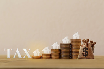 Mini house on rows of rising coins, US dollar bags, word tax on wood table. House or housing, land...