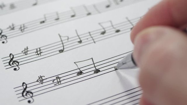 The hand of an unknown musician writes the notes of a composition on a pentagram. Fountain pen and notes in macro. Music and creativity. Hobbies.