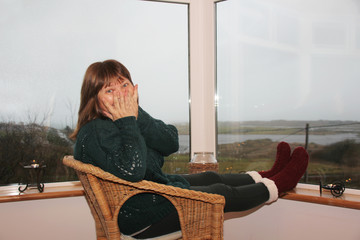 woman sits in a cozy wicker chair on a bright covered veranda in the mountains, enjoys relaxing,...