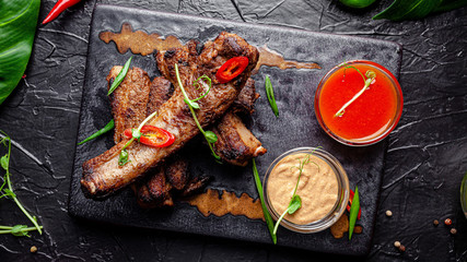 Mexican cuisine. Grilled pork ribs with hot pepper, white and red sauce. Serving dishes in a restaurant on a black plate. background image, copy space text
