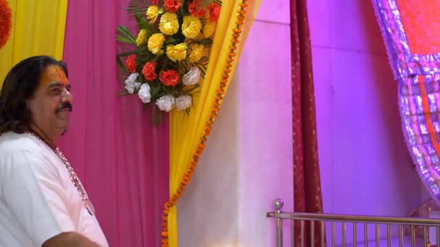 Old Brahmin in traditional clothing worshipping the god in a decorated Indian temple / mandir. Pan shot of an Indian priest doing Aarti / Puja with burning lamp in the temple of Goddess Durga (Sher...