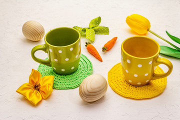 Easter table setting on textured white putty background. Spring holiday card template. Cutlery, knitted napkin, eggs, carrot, bunny, tulip, polka dot cups