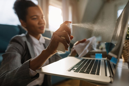 Close-up of black businesswoman cleaning laptop while working at home.